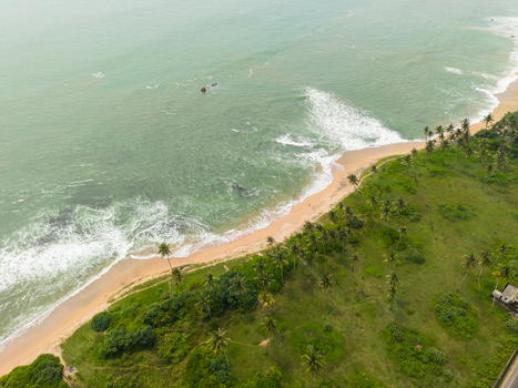Aerial view of the tropical coastline with turquoise waves crashing on a sandy beach lined with palm trees and lush greenery in Galle Southern Province Sri Lanka. Aerial view of the tropical coastline with turquoise waves crashing on a sandy beach lined with palm trees and lush greenery in Galle Southern Province Sri Lanka.