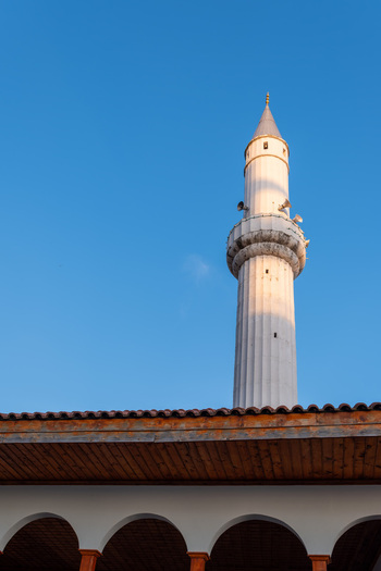 View of the white minaret of a mosque rising above a wooden roof with arches under a clear blue sky in Kruje Durres County Albania.