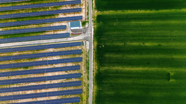 Aerial view of rows of solar panels in a photovoltaic power station adjacent to a lush green agricultural field separated by a rural road Sabac Vojvodina Serbia.