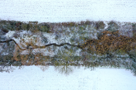 Aerial view of a winding stream flowing through a row of trees and shrubs amidst snow covered fields Forchheim Bavaria Germany.