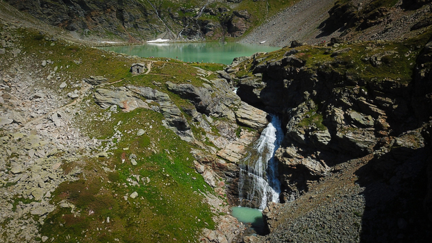 Aerial view of the cascade s waters plunging into a turquoise pool below against the backdrop of Lago di San Grato Valgrisenche Aosta Valley Italy.