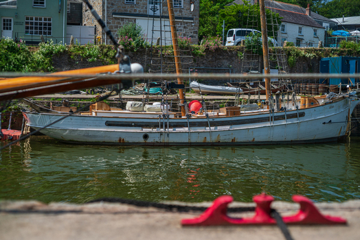 View of a white wooden sailing boat moored in the historic harbor with stone quay walls and traditional buildings in the background Charlestown Cornwall United Kingdom. View of a white wooden sailing boat moored in the historic harbor with stone quay walls and traditional buildings in the background Charlestown Cornwall United Kingdom.