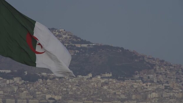 Aerial view of Algerian flag waving over a hillside city Algeria.