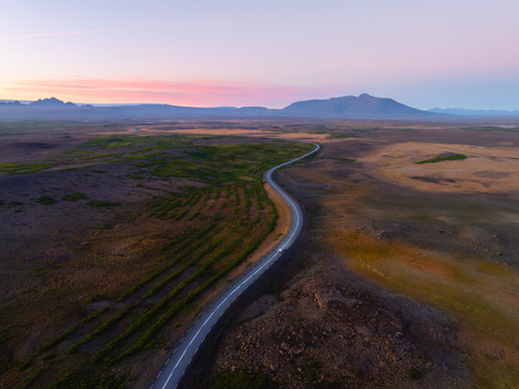 Aerial view of a winding road cutting through a vast landscape under a pastel sky Reykholt Iceland.