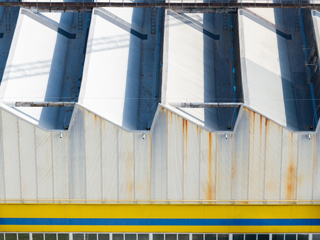 Aerial view of an agricultural machinery production facility featuring a sawtooth roof design with metal siding and a yellow and blue painted wall in Plock Mazowieckie Poland. Aerial view of an agricultural machinery production facility featuring a sawtooth roof design with metal siding and a yellow and blue painted wall in Plock Mazowieckie Poland.