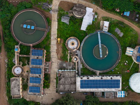 Aerial view of a water treatment plant featuring circular sedimentation tanks and solar panels installed on building rooftops in Karad Maharashtra India.