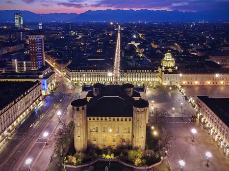 Aerial view of Palazzo Madama and Piazza Castello with illuminated city streets and the Alps under a twilight sky in Turin Piedmont Italy.