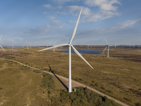 Aerial view of the Eaglesham moor wind farm featuring large white turbines and a blue lake under a bright sky Kilmarnock Scotland United Kingdom.