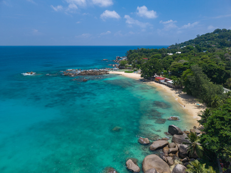 Aerial view of turquoise waters gently kissing the sandy shore where granite boulders rest as lush greenery meets the horizon Vista do Mar Mahe island Seychelles. Aerial view of turquoise waters gently kissing the sandy shore where granite boulders rest as lush greenery meets the horizon Vista do Mar Mahe island Seychelles.