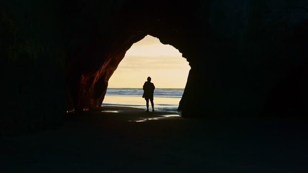View of a person in a cave opening looking at the ocean New Zealand. View of a person in a cave opening looking at the ocean New Zealand.