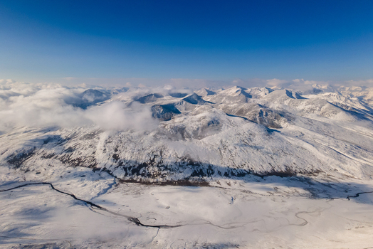 Aerial view of the snow covered peaks of Babusar Pass with clouds drifting over the rugged mountain landscape and a winding road in the valley Babusar KPK Pakistan.