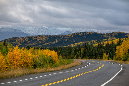View of Denali National Park and Preserve with a winding road leading towards snow capped mountains surrounded by autumn foliage and evergreen trees in Alaska United States. View of Denali National Park and Preserve with a winding road leading towards snow capped mountains surrounded by autumn foliage and evergreen trees in Alaska United States.