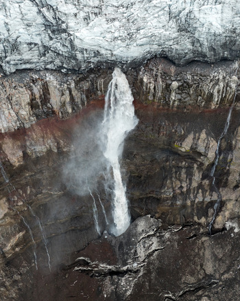 Aerial view of Langjokull glacier waterfall cascading down dark volcanic rock cliffs in Vik Myrdalshreppur Iceland.