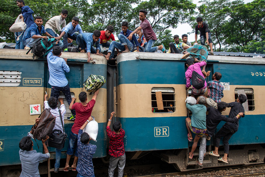 Dhaka Bangladesh 14 June 2018 View of people climbing onto a crowded train at Airport Railway Station with passengers hanging from doors and sitting on the roof. Dhaka Bangladesh 14 June 2018 View of people climbing onto a crowded train at Airport Railway Station with passengers hanging from doors and sitting on the roof.