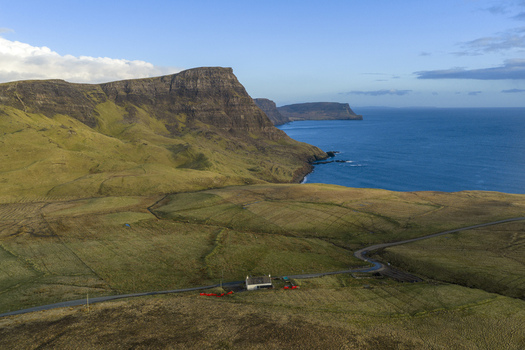 Aerial view of a camper parked near a remote cottage on the rugged coastline with dramatic cliffs and the blue sea Isle of Skye United Kingdom. Aerial view of a camper parked near a remote cottage on the rugged coastline with dramatic cliffs and the blue sea Isle of Skye United Kingdom.