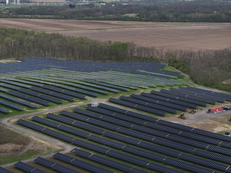 Lebanon United States 12 April 2026 Aerial view of a large solar farm with rows of blue photovoltaic panels surrounded by green trees and brown agricultural fields.