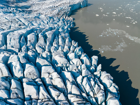 Aerial view of a massive glacier edge with deep crevasses and jagged ice formations meeting the dark waters of a glacial lake filled with floating icebergs in Iceland. Aerial view of a massive glacier edge with deep crevasses and jagged ice formations meeting the dark waters of a glacial lake filled with floating icebergs in Iceland.