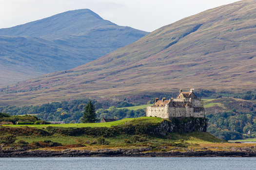 View of Duart Castle a historic stone fortress perched on a rocky cliff with rolling hills and mountains in the background Isle of Mull Scotland United Kingdom.