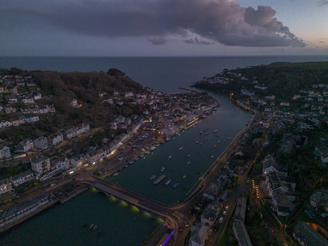 Aerial view of the coastal town of Looe at dusk featuring the Banjo Pier moored boats in the river estuary and surrounding hillsides with residential buildings in Looe Cornwall United Kingdom. Aerial view of the coastal town of Looe at dusk featuring the Banjo Pier moored boats in the river estuary and surrounding hillsides with residential buildings in Looe Cornwall United Kingdom.