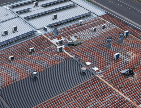 Melbourne VIC Australia 25 September 2026 Aerial view of an industrial building roof featuring corrugated metal sheets rusted sections solar panels and various HVAC ventilation units.