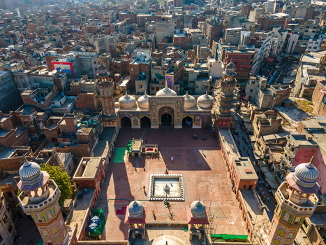 Aerial view of Wazir Khan Mosque featuring its intricate tile work minarets and central courtyard surrounded by the dense urban fabric of Lahore Punjab Pakistan.