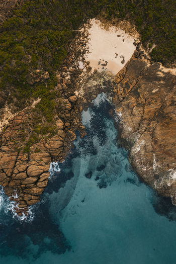 Aerial view of Conspicuous Cliff featuring rugged rock formations a secluded sandy beach and turquoise ocean waters in Nornalup Western Australia Australia. Aerial view of Conspicuous Cliff featuring rugged rock formations a secluded sandy beach and turquoise ocean waters in Nornalup Western Australia Australia.