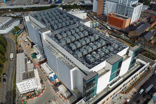 Aerial view of a large modern data center with numerous rooftop cooling units and HVAC systems surrounded by industrial infrastructure and roads in the United Kingdom. Aerial view of a large modern data center with numerous rooftop cooling units and HVAC systems surrounded by industrial infrastructure and roads in the United Kingdom.