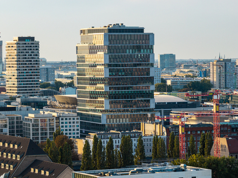 Aerial view of a modern glass office tower rising above the urban skyline of Berlin featuring surrounding buildings construction cranes and clear light in Berlin Berlin Germany. Aerial view of a modern glass office tower rising above the urban skyline of Berlin featuring surrounding buildings construction cranes and clear light in Berlin Berlin Germany.