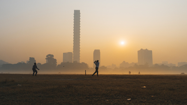 View of cricket players silhouetted in the early morning light against the backdrop of Kolkata s skyline shrouded in a golden haze Kolkata West Bengal India. View of cricket players silhouetted in the early morning light against the backdrop of Kolkata s skyline shrouded in a golden haze Kolkata West Bengal India.