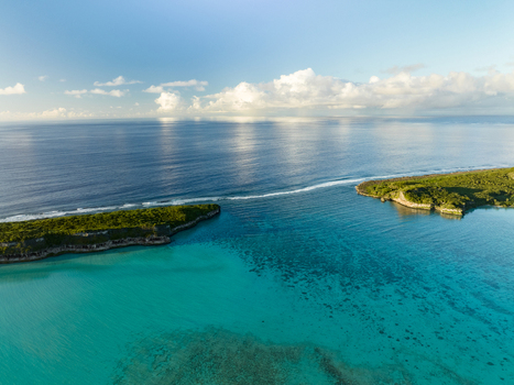 Aerial view of the channel where turquoise waters meet the deep blue sea framed by lush green islands under a sky of scattered clouds Ouvéa Loyalty Islands Province New Caledonia. Aerial view of the channel where turquoise waters meet the deep blue sea framed by lush green islands under a sky of scattered clouds Ouvéa Loyalty Islands Province New Caledonia.