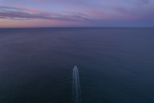 Aerial view of a small boat leaving a wake in the calm ocean during a colorful sunset in Faro District Portugal. Aerial view of a small boat leaving a wake in the calm ocean during a colorful sunset in Faro District Portugal.