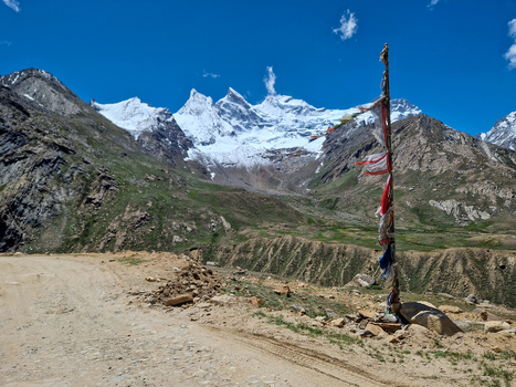 View of Penzi La road with prayer flags in the foreground and snow capped mountains under a clear blue sky in Zanskar Ladakh India.