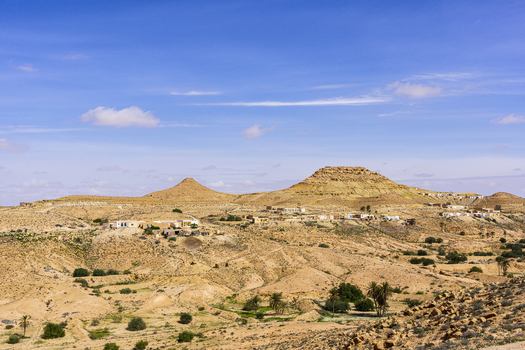 View of the desert landscape and traditional buildings with arid hills rocky terrain and a clear blue sky in Tataouine Tataouine Governorate Tunisia.