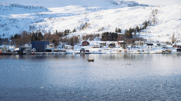 View of a solitary boat glides across the serene icy waters mirroring the snow dusted village embraced by majestic mountains under a crisp clear sky Brensholmen Troms Norway. View of a solitary boat glides across the serene icy waters mirroring the snow dusted village embraced by majestic mountains under a crisp clear sky Brensholmen Troms Norway.