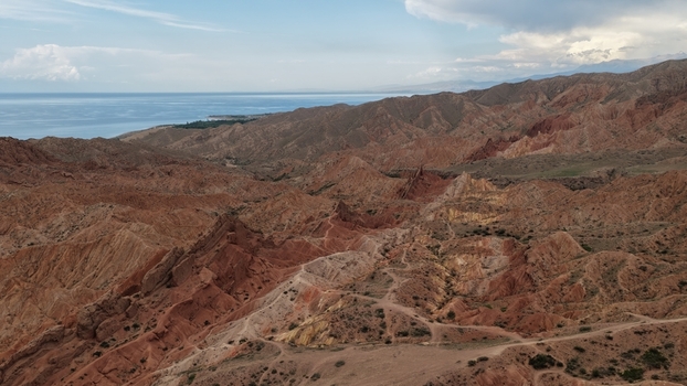 Aerial view of Jety Oguz red sandstone rock formations with rugged terrain winding trails and the distant Issyk Kul lake in Jety Oguz Issyk Kul Region Kyrgyzstan. Aerial view of Jety Oguz red sandstone rock formations with rugged terrain winding trails and the distant Issyk Kul lake in Jety Oguz Issyk Kul Region Kyrgyzstan.