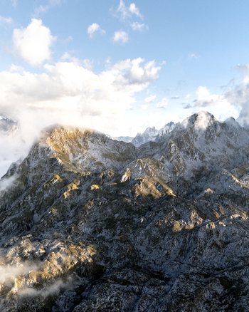 Aerial view of rugged rocky peaks pierce through a veil of ethereal clouds under a bright sky Picos de Europa Asturias Spain. Aerial view of rugged rocky peaks pierce through a veil of ethereal clouds under a bright sky Picos de Europa Asturias Spain.