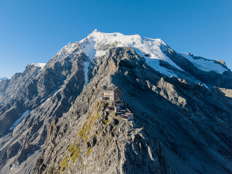 Aerial view of Payer Hutte perched on a rocky ridge of Ortler Mountain with snow capped peaks and clear blue sky in Sulden Trentino Alto Adige Italy. Aerial view of Payer Hutte perched on a rocky ridge of Ortler Mountain with snow capped peaks and clear blue sky in Sulden Trentino Alto Adige Italy.