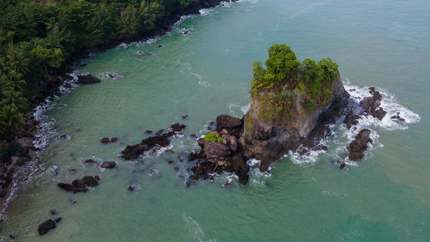 Aerial view of the iconic Karang Agung rock formation with lush greenery surrounded by turquoise sea water and rocky shores in Ayah Central Java Indonesia. Aerial view of the iconic Karang Agung rock formation with lush greenery surrounded by turquoise sea water and rocky shores in Ayah Central Java Indonesia.