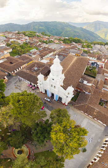 Aerial view of a white church with blue accents stands prominently amidst the terracotta rooftops of the town nestled against a backdrop of verdant mountains Salamina Caldas Colombia. Aerial view of a white church with blue accents stands prominently amidst the terracotta rooftops of the town nestled against a backdrop of verdant mountains Salamina Caldas Colombia.