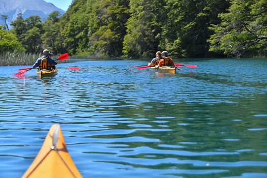 View of people kayaking on the calm blue waters of Nahuel Huapi Lake surrounded by lush green forests and mountains in San Carlos de Bariloche Rio Negro Argentina. View of people kayaking on the calm blue waters of Nahuel Huapi Lake surrounded by lush green forests and mountains in San Carlos de Bariloche Rio Negro Argentina.