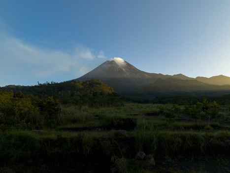 Aerial view of Bunker Kaliadem Merapi and the smoking peak of Mount Merapi volcano surrounded by lush green forests under a clear sky in Kecamatan Pakem Daerah Istimewa Yogya Indonesia. Aerial view of Bunker Kaliadem Merapi and the smoking peak of Mount Merapi volcano surrounded by lush green forests under a clear sky in Kecamatan Pakem Daerah Istimewa Yogya Indonesia.