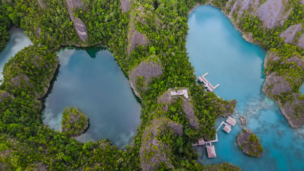 Aerial view of turquoise lagoons surrounded by lush karst cliffs and wooden overwater bungalows in Indonesia. Aerial view of turquoise lagoons surrounded by lush karst cliffs and wooden overwater bungalows in Indonesia.
