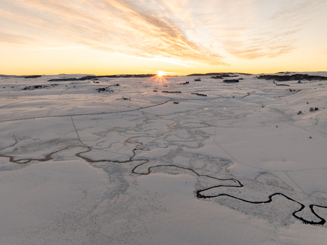 Aerial view of the serpentine river meanders through the snowy expanse under the golden glow of the setting sun Nasbinals Occitanie France.