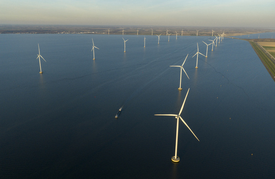 Aerial view of an offshore wind farm with white turbines standing in blue water under a clear sky in the Netherlands. Aerial view of an offshore wind farm with white turbines standing in blue water under a clear sky in the Netherlands.