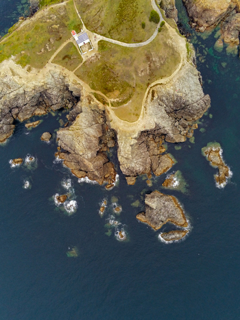 Aerial view of Pointe des Poulains lighthouse on the rugged coastline with rocky cliffs winding paths and deep blue Atlantic ocean waters in Sauzon Bretagne France. Aerial view of Pointe des Poulains lighthouse on the rugged coastline with rocky cliffs winding paths and deep blue Atlantic ocean waters in Sauzon Bretagne France.
