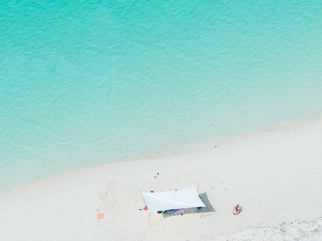 Aerial view of turquoise water meeting the pristine white sands with a lone white tent standing out against the bright beach Thuraakunu Thiladhunmathee Uthuruburi Maldives. Aerial view of turquoise water meeting the pristine white sands with a lone white tent standing out against the bright beach Thuraakunu Thiladhunmathee Uthuruburi Maldives.