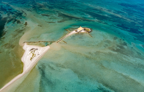 Aerial view of a small island with a church surrounded by turquoise shallow waters and a sandy spit in Lefkada Greece.