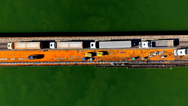 Aerial view of the Smederevo bridge and shipyard featuring heavy trucks and maintenance equipment on an orange surfaced deck over green river water Smederevo Podunavlje District Serbia.