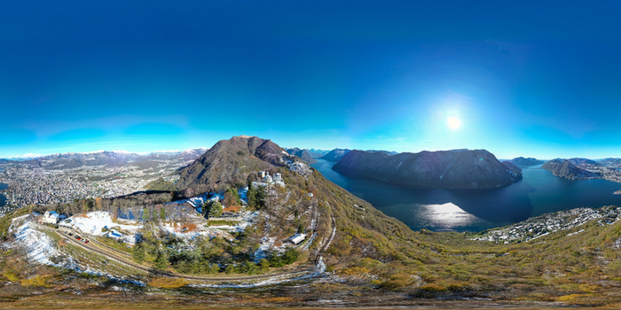 Aerial view of the panoramic landscape of Lake Lugano and surrounding snow dusted mountains under a clear blue sky Lugano Ticino Switzerland.
