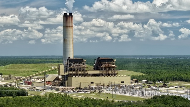 Aerial view of the Seminole Electric Cooperative power plant with a tall smokestack industrial buildings and surrounding forests under a blue sky in Palatka Florida United States.